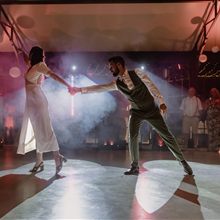 Ouverture de bal : les mariés dansent main dans la main dans la fumée et les lumières